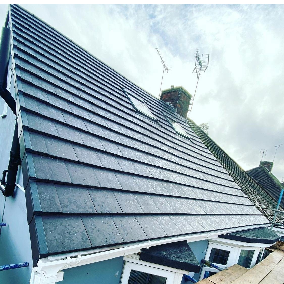 A newly tiled roof in dark grey tiles against a blue sky